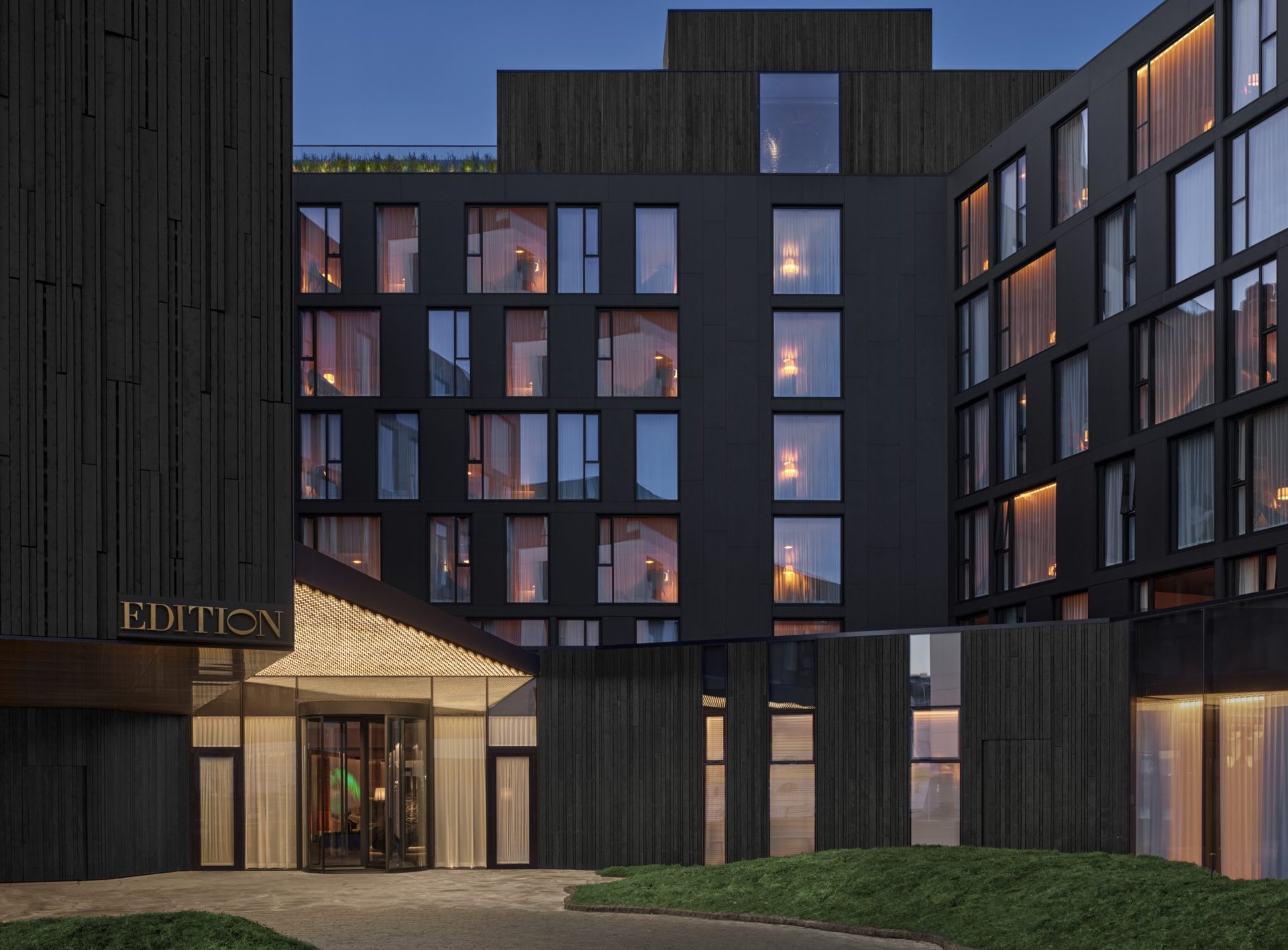 The dark timber façade and lit entrance of The Reykjavik EDITION at dusk